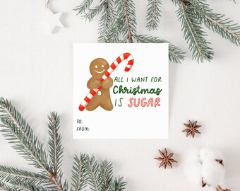 Op de afbeelding: Een wit cadeau-etiket met een peperkoekman die een snoepstok houdt. Het etiket zegt "Alles wat ik voor kerst wil is suiker". Er is ruimte om "Aan :" en "Van :" op het etiket te schrijven.
