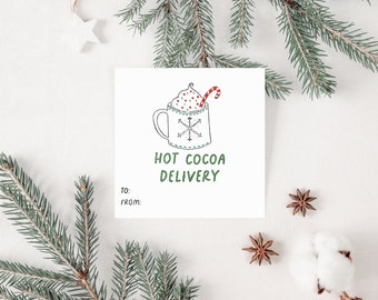 Op de afbeelding: Een witte kaart met een handgetekend plaatje van een mok met warme chocolademelk met slagroom en een snoepstok. De tekst "HOT COCOA DELIVERY" staat in het groen onder de mok. De kaart heeft lege regels voor "Aan:" en "Van:".