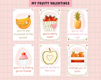 Op de afbeelding: Zes printbare Valentijnsdagkaarten met fruitwoordspelingen. De kaarten zijn wit met gouden randen en roze harten. De kaarten bevatten illustraties van bananen, aardbeien, een ananas, een cupcake, een appel en sinaasappelen.