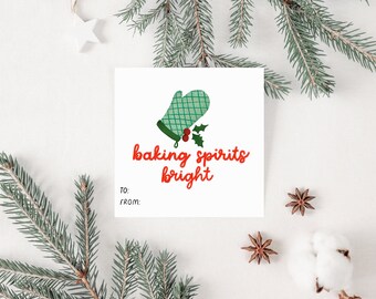Op de afbeelding: Een wit cadeau-etiket met een groene ovenwant en een hulst-illustratie. De tekst "baking spirits bright" is geschreven in rood cursief. Het etiket heeft lege ruimtes voor "Aan :" en "Van :" .
