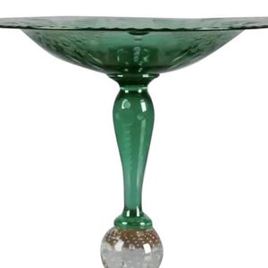 May include: A green glass pedestal bowl with a wide, textured rim. The bowl sits atop a slender stem with a bulbous, bubble-filled section near the base. The base is a flat, circular foot.