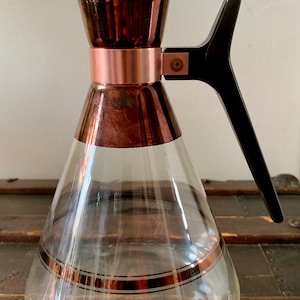 May include: A clear glass jug with a copper-coloured lid and handle. The jug has two gold bands around the middle.