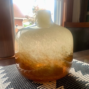 Peut inclure: Un vase en verre blanc et brun avec une surface texturée. Le vase a un corps arrondi et un col étroit.