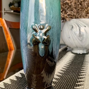 Peut inclure: Un vase en céramique avec un glaçage vert foncé et brun. Le vase a un design unique avec un motif floral en relief tridimensionnel.