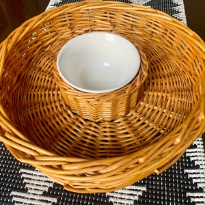 May include: A woven wicker serving tray with a white ceramic bowl in the centre. The tray is made of natural brown wicker and has a round shape.