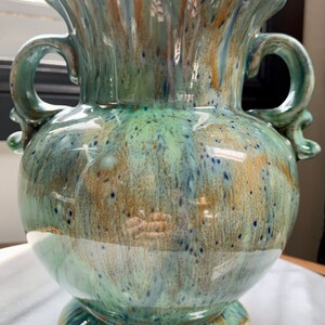 May include: A green and brown ceramic vase with a fluted top and two handles. The vase has a speckled glaze with a mottled effect.
