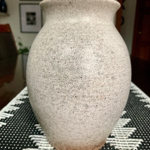 May include: A white ceramic vase with a speckled texture. The vase has a rounded body and a slightly flared opening.