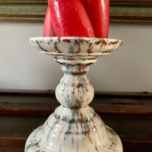 Peut inclure: Un bougeoir en céramique blanche avec un motif de peinture éclaboussée dans des tons de vert, bleu et rouge. Le bougeoir a une base ronde et une seule tige ornée.