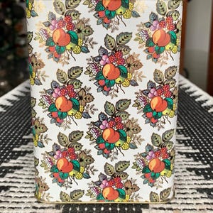 May include: A white rectangular tin with a gold trim. The tin has a repeating pattern of red, orange, yellow, green, and purple fruit and leaves on a white background.