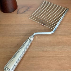 May include: Silver-plated cake comb with a long, rectangular handle and a series of parallel tines. The handle features ornate detailing. The comb is designed for cutting and serving cakes.