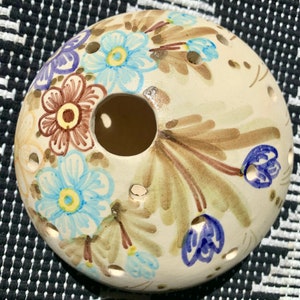 Puede incluir: Un plato de cerámica blanco en forma de huevo con un agujero en el centro. El plato está decorado con flores pintadas a mano en marrón, azul y morado.