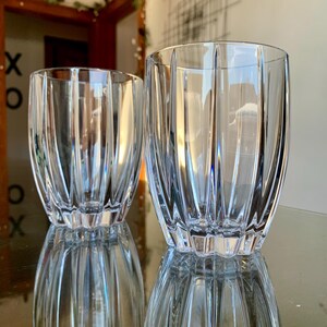 May include: Two clear, ribbed drinking glasses. The glasses have a cylindrical shape with vertical grooves, reflecting light and creating a textured appearance. The glasses are on a reflective surface.