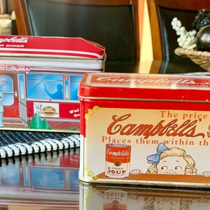 May include: Two vintage red and white Campbell's Soup tin boxes. The larger box features a diner scene with the text "Campbells Soups Corner Diner". The smaller box features a girl peeking over the top of a can of Campbell's Soup with the text "The price of Campbells SOUPS Places them within the reach of all 21 kinds - 10¢ a Can".