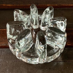 May include: A clear glass coaster with a circular design. The coaster has eight sections, each with a raised, rounded edge. The coaster is designed to hold multiple glasses or mugs.