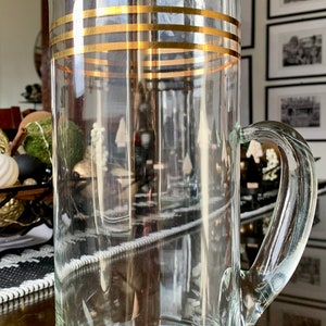 May include: A clear glass pitcher with a gold band around the top. The pitcher has a handle and a spout.