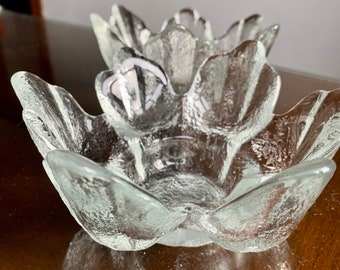 May include: Two clear glass candle holders shaped like a flower with five petals. The holders are textured and have a frosted appearance.