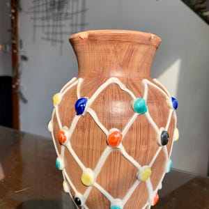 Peut inclure: Un vase en céramique marron avec une texture imitation bois, orné d'un motif en treillis blanc en relief. De petites perles circulaires brillantes et multicolores, bleues, orange, jaunes, turquoise et noires, sont fixées aux intersections.