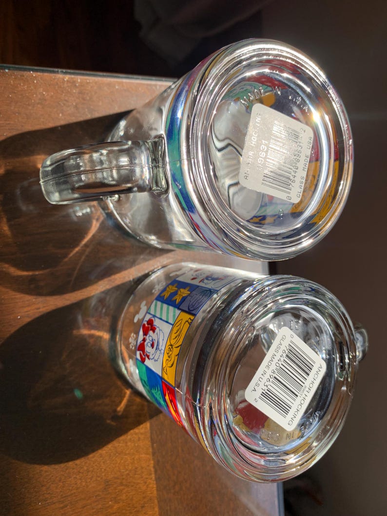 Może przedstawiać: Dwa przezroczyste kubki szklane z kolorowymi wzorami z kresk&oacute;wek i białą naklejką z kodem kreskowym i tekstem "Anchor Hocking Glass Made in USA" na spodzie.