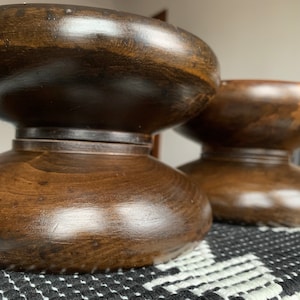 May include: Two dark brown wooden pedestal bases with a smooth, polished finish. The bases are round and have a slight curve to them.