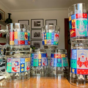 May include: Set of eight glass mugs featuring a colorful patchwork design with various Disney characters, including Mickey Mouse and Minnie Mouse. The mugs are perfect for enjoying hot beverages.