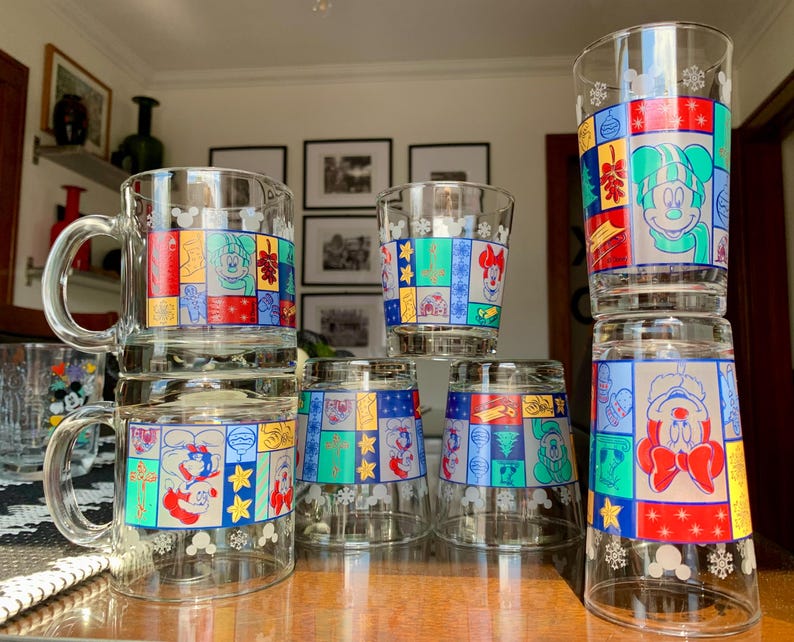 May include: Set of eight glass mugs featuring a colorful patchwork design with various Disney characters, including Mickey Mouse and Minnie Mouse. The mugs are perfect for enjoying hot beverages.