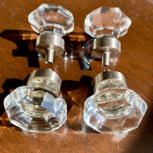 Peut inclure: Quatre boutons de meuble en verre clair et facetté avec des bases en nickel brossé. Les boutons ont un design classique et élégant, parfait pour ajouter une touche de sophistication aux meubles ou aux armoires. Les boutons sont disposés en carré.
