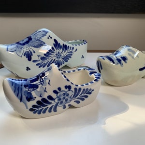 May include: Three blue and white Delftware ceramic clogs, each with a different design. The clogs are traditional Dutch souvenirs.