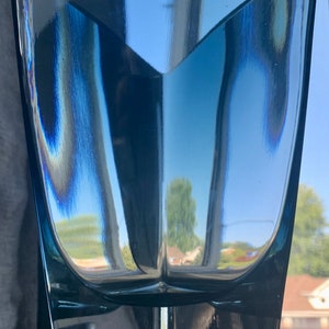 May include: A clear blue glass vase with a geometric design. The vase has a wide base and a narrow neck.