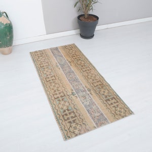May include: A beige and brown patterned runner rug with a light blue and green border. The rug has a distressed look and is perfect for adding a touch of vintage style to your home.