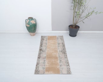 Puede incluir: Un tapete corredor beige y gris con un patrón y una franja central de color marrón claro. El tapete está sobre un suelo blanco.