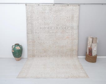 May include: A large, off-white rug with a faded floral pattern. The rug is hanging on a wall and has a distressed, vintage look.