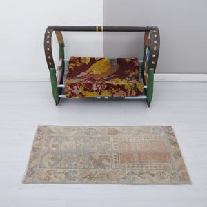 May include: A small, rectangular rug with a beige, cream, and light brown pattern. The rug is in front of a wooden crib with a colorful patterned mattress.
