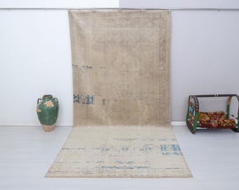 Könnte beinhalten: Ein Vintage-Teppich mit einem verblassten, hellbeigen Hintergrund und einem dezenten blau-weißen Muster. Der Teppich hat einen Used-Look und ist perfekt, um jedem Raum einen Hauch von rustikalem Charme zu verleihen.