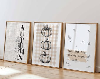 Könnte beinhalten: Drei gerahmte Kunstdrucke mit Holzrahmen. Der linke Druck zeigt vertikal "AUTUMN". Der mittlere Druck hat drei Kürbisillustrationen auf einem karierten Hintergrund in Beige und Weiß. Der rechte Druck zeigt "And then the leaves began to fall.." mit Blätterillustrationen.