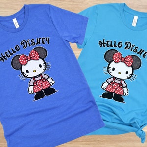 May include: Two blue and turquoise t-shirts with a Hello Disney graphic featuring a cartoon character with red polka dot bow and red polka dot dress.