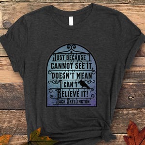 Pode incluir: Uma camiseta cinza escura com uma estampa gr&aacute;fica de um p&aacute;ssaro preto em uma gaiola. O texto na estampa diz "Just because cannot see it, doesn't mean can't believe it!" e "Jack Skellington".