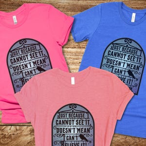 Pode incluir: Tr&ecirc;s t-shirts com um design gr&aacute;fico preto e branco com um corvo e o texto "Just because cannot see it, doesn't mean I can't believe it!"