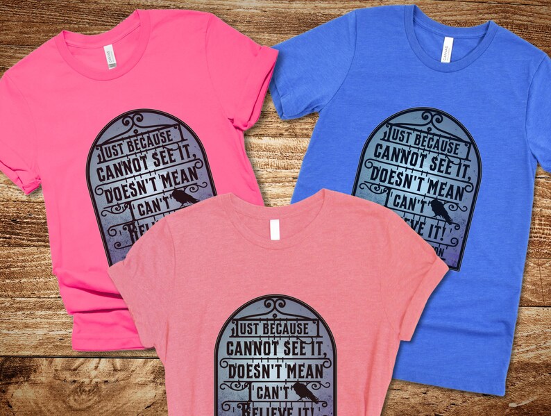 Pode incluir: Tr&ecirc;s t-shirts com um design gr&aacute;fico preto e branco com um corvo e o texto "Just because cannot see it, doesn't mean I can't believe it!"