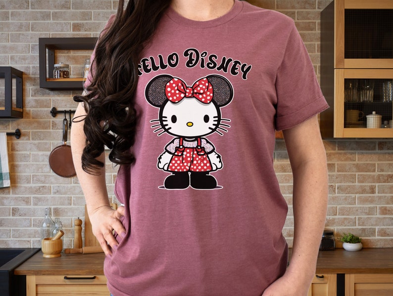 May include: A maroon t-shirt with the text "Hello Disney" printed on the front. A cartoon image of a character with black and white polka dot ears and a red and white polka dot dress is printed below the text.