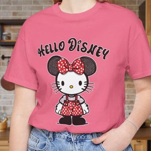May include: Pink t-shirt with a black and white cartoon image of Hello Kitty wearing a red bow and a red and white polka dot dress. The text "Hello Disney" is printed in black on the shirt.