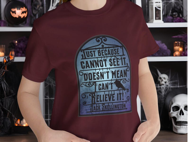 Pode incluir: Camiseta vinho com um gr&aacute;fico azul e branco de uma l&aacute;pide com o texto "Just because cannot see it, doesn't mean I can't believe it!" e "Jack Skellington".