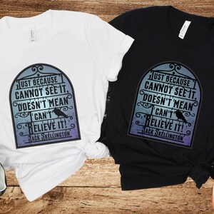 Pode incluir: Duas camisetas com uma estampa gr&aacute;fica em preto e branco de um port&atilde;o com um corvo e o texto "Just because cannot see it, doesn't mean I can't believe it! Jack Skellington". Uma camiseta &eacute; branca e a outra &eacute; preta.