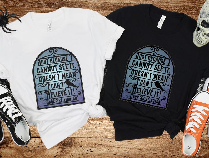 Pode incluir: Duas camisetas com uma estampa gr&aacute;fica em preto e branco de um port&atilde;o com um corvo e o texto "Just because cannot see it, doesn't mean I can't believe it! Jack Skellington". Uma camiseta &eacute; branca e a outra &eacute; preta.