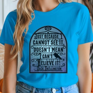 Pode incluir: Uma camiseta azul turquesa com uma estampa gr&aacute;fica em preto e branco de uma cita&ccedil;&atilde;o dentro de uma moldura decorativa. A cita&ccedil;&atilde;o diz "Just because cannot see it, doesn't mean I can't believe it!" com o nome "Jack Skellington" na parte inferior.