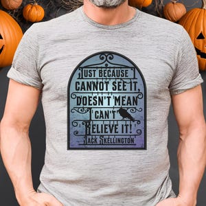 Pode incluir: Uma camiseta cinza com um gr&aacute;fico preto e branco de um port&atilde;o com o texto "Just because I cannot see it, doesn't mean I can't believe it! Jack Skellington"