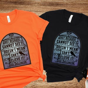 Pode incluir: Duas camisetas com uma estampa gr&aacute;fica em preto e branco de uma placa com o texto "Just because cannot see it, doesn't mean I can't believe it! Jack Skellington". As camisetas s&atilde;o laranja e preta.