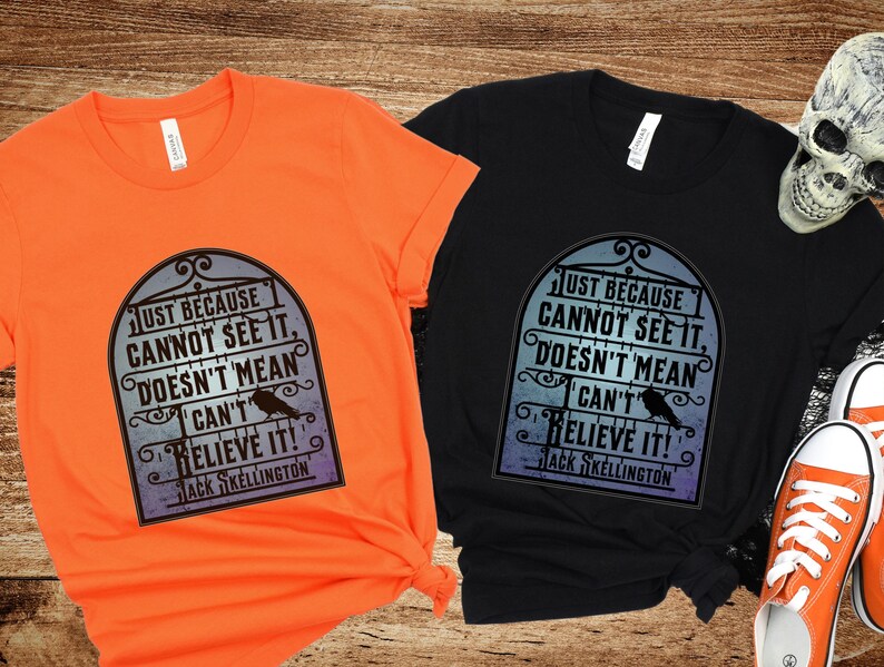 Pode incluir: Duas camisetas com uma estampa gr&aacute;fica em preto e branco de uma placa com o texto "Just because cannot see it, doesn't mean I can't believe it! Jack Skellington". As camisetas s&atilde;o laranja e preta.