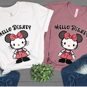 May include: Two t-shirts with a Hello Disney graphic featuring a Hello Kitty character with Minnie Mouse ears and a red polka dot bow. The t-shirts are white and pink.