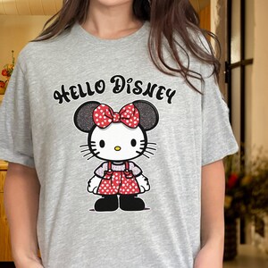 May include: Gray t-shirt with a Hello Disney graphic featuring a cartoon character with red polka dot overalls and a red bow.