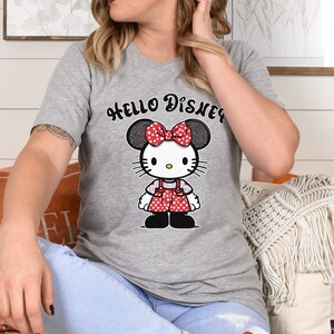 May include: Gray t-shirt with a cartoon image of Hello Kitty wearing a red bow and a red and white polka dot dress. The text "HELLO DISNEY" is printed above the image.